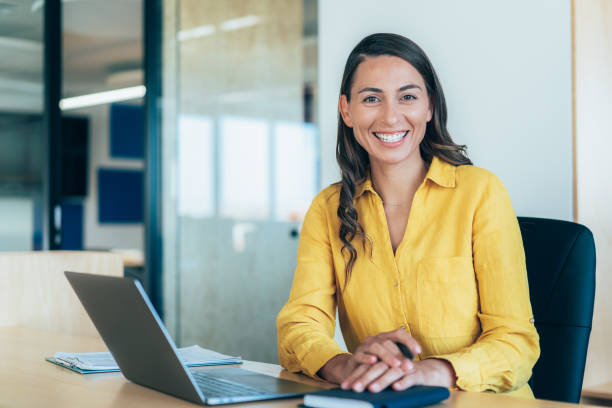 Confident businesswoman working on laptop at her workplace at modern office. Portrait of businesswoman in front of her laptop, looking at camera.